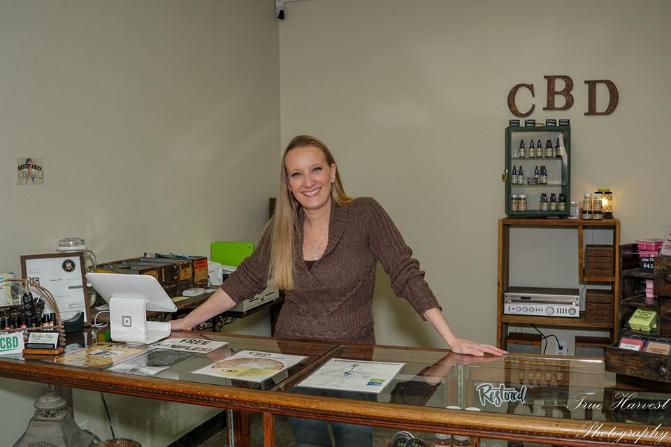 Rachel, owner of Rustic Oils, standing behind showcase in a rustic & cozy store