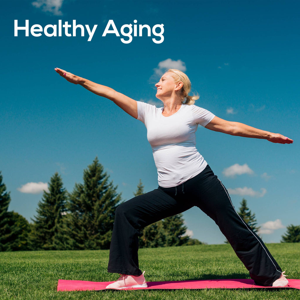 A woman in a white t-shirt and black pants performs a yoga pose on a pink mat in a grassy park under a blue sky, with the text 'Healthy Aging' in the top left corner.