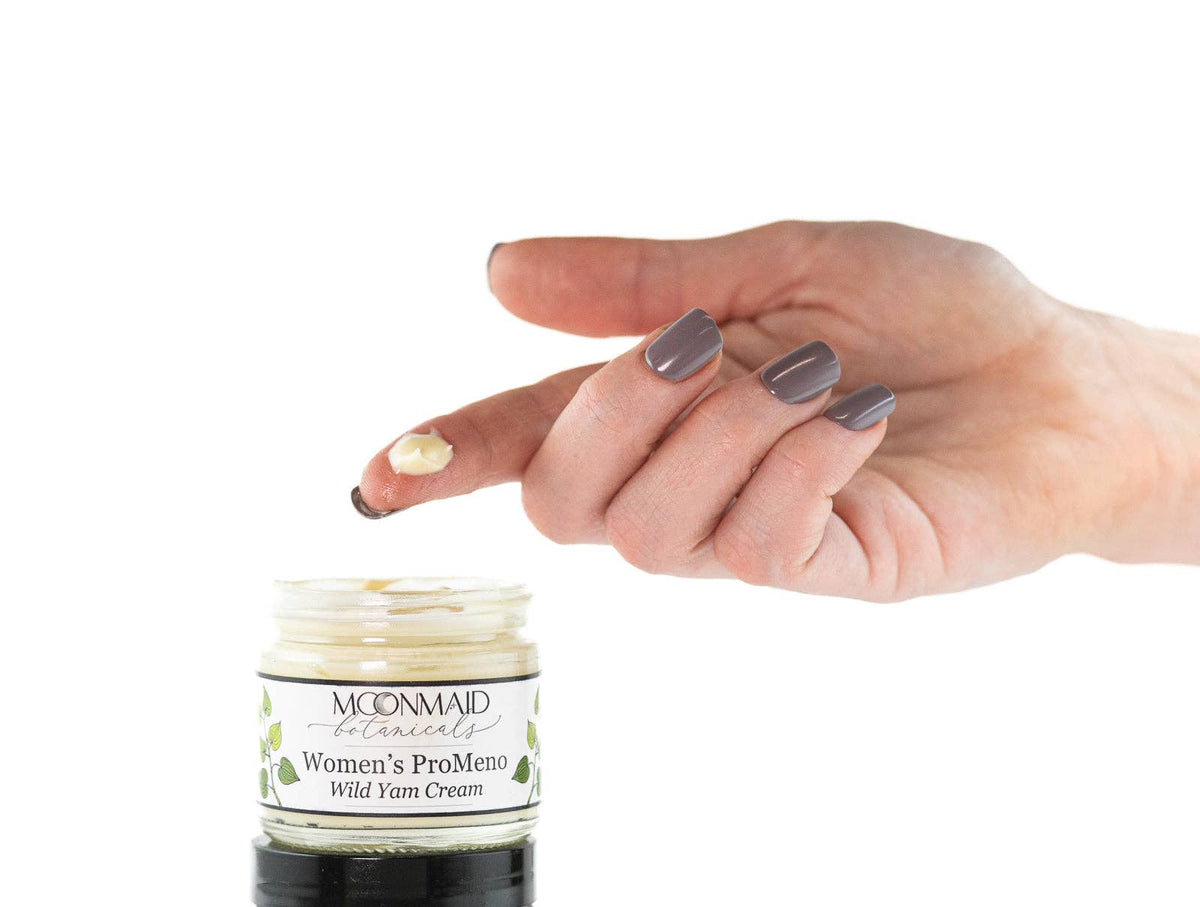 Hand holding a jar of Women's ProMeno Wild Yam Cream with a white background.  Image shows pea sized amount indicating application size