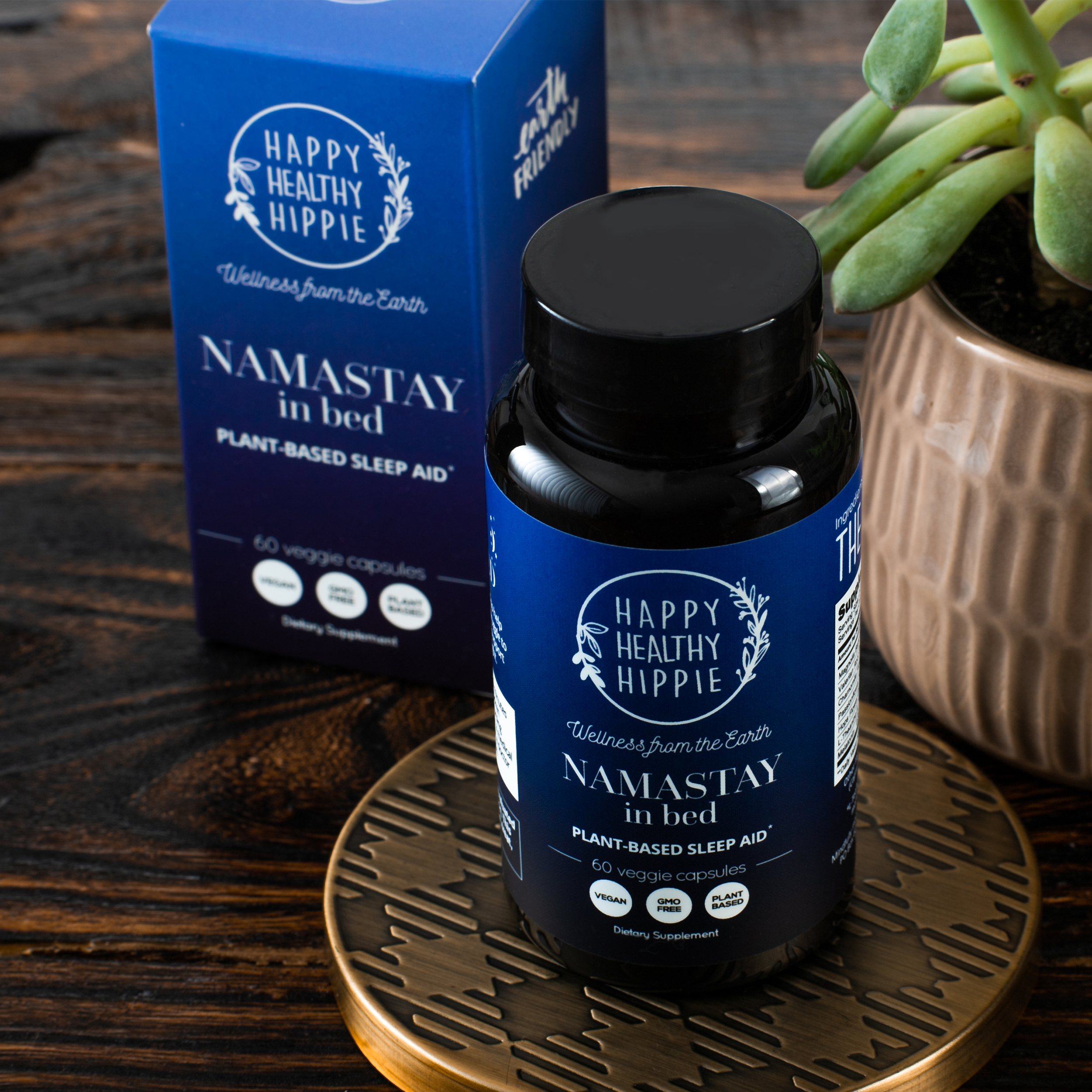 Happy Healthy Hippie Namastay in bed plant-based sleep aid bottle and packaging on a wooden surface with a plant.