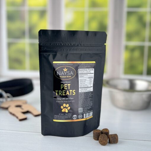 A package of Naysa brand pet treats with CBD, featuring a black pouch with product information, alongside several treat chews displayed in front of the package.