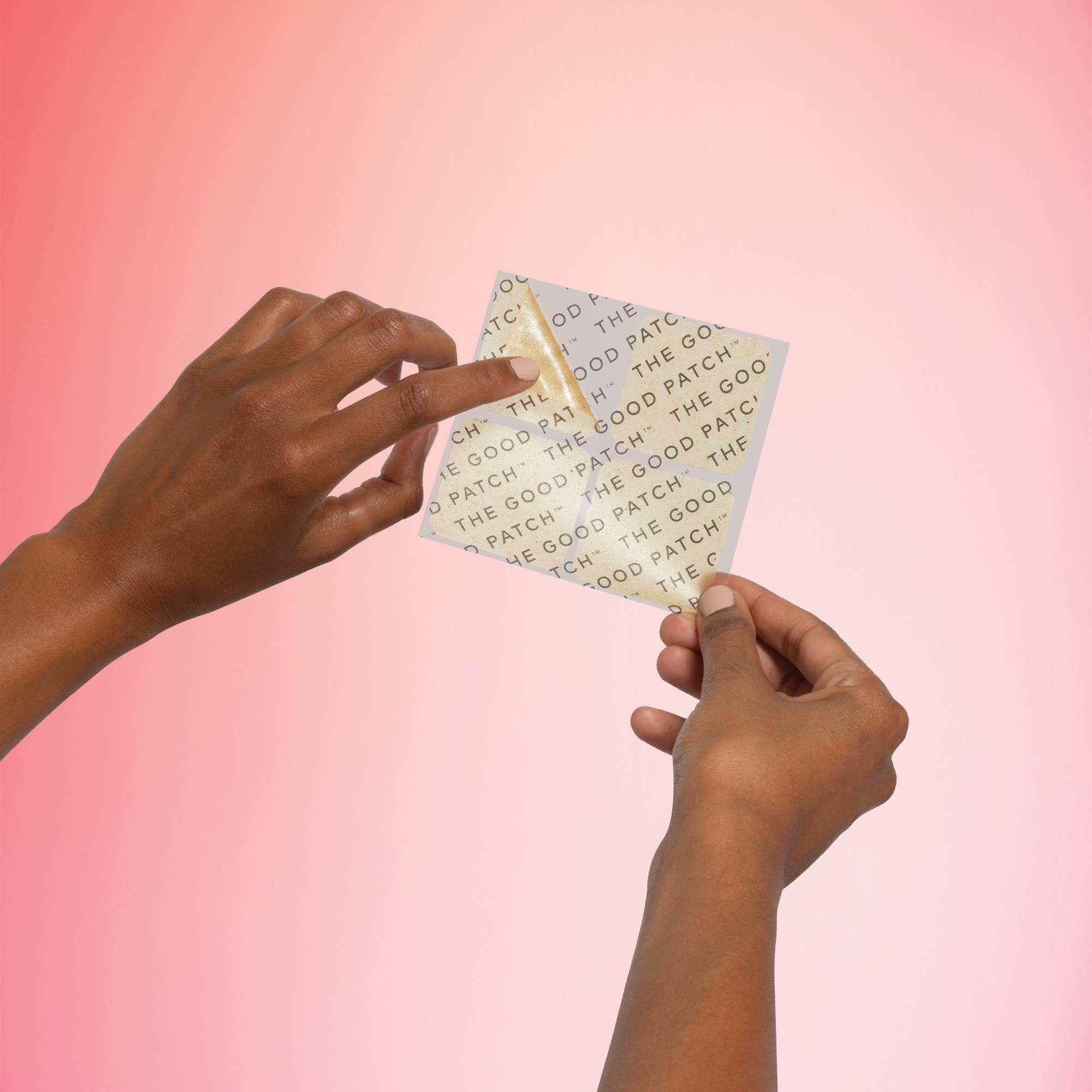 Two hands holding a folded piece of paper with 'The Good Patch' branding against a pink gradient background.