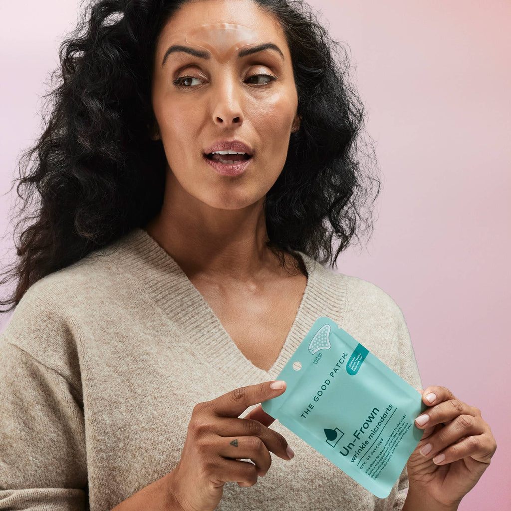 Woman holding a skincare product package against a pink background