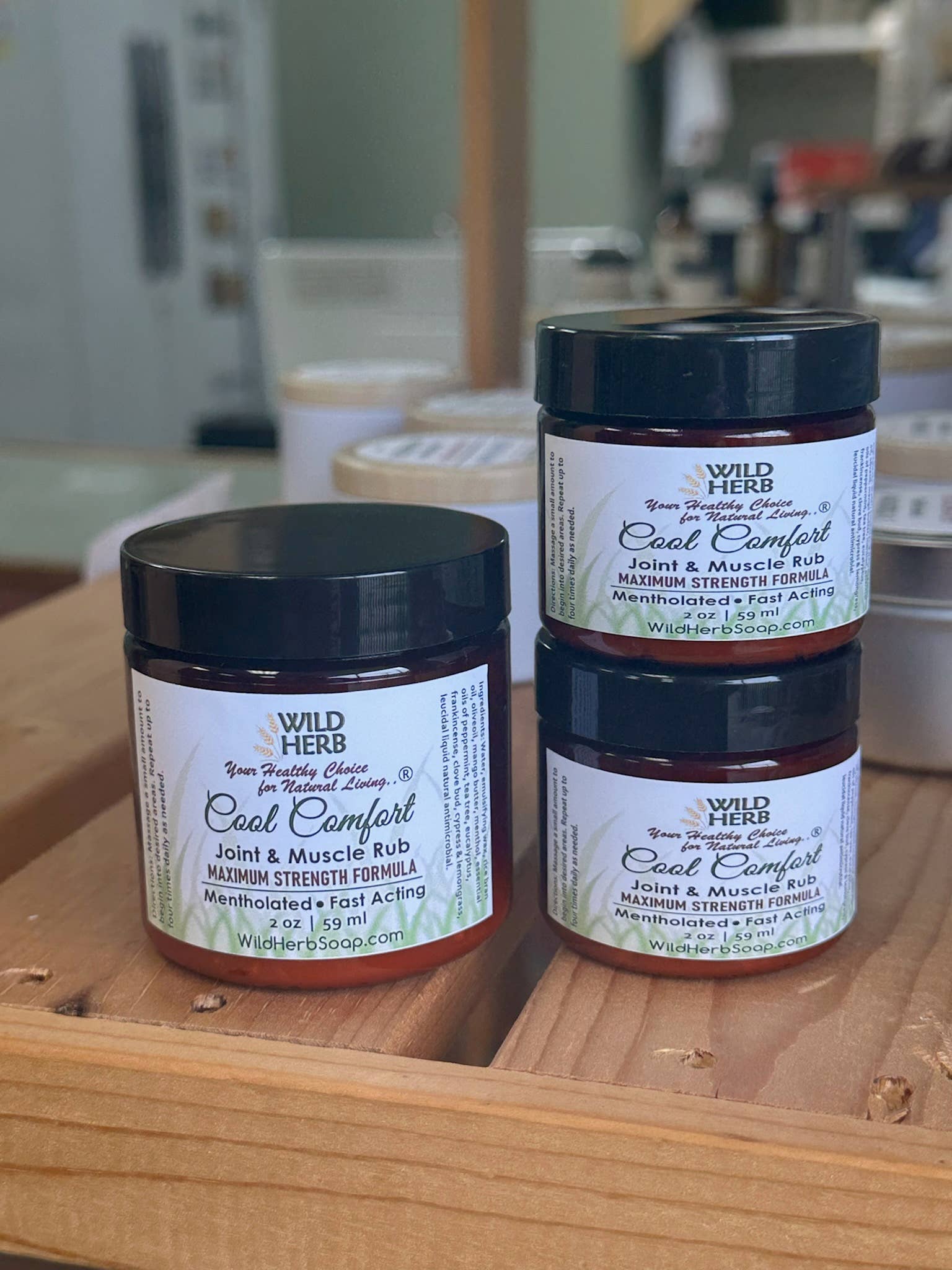 Three jars of Wild Herb Cool Comfort on a wooden surface with a blurred background.