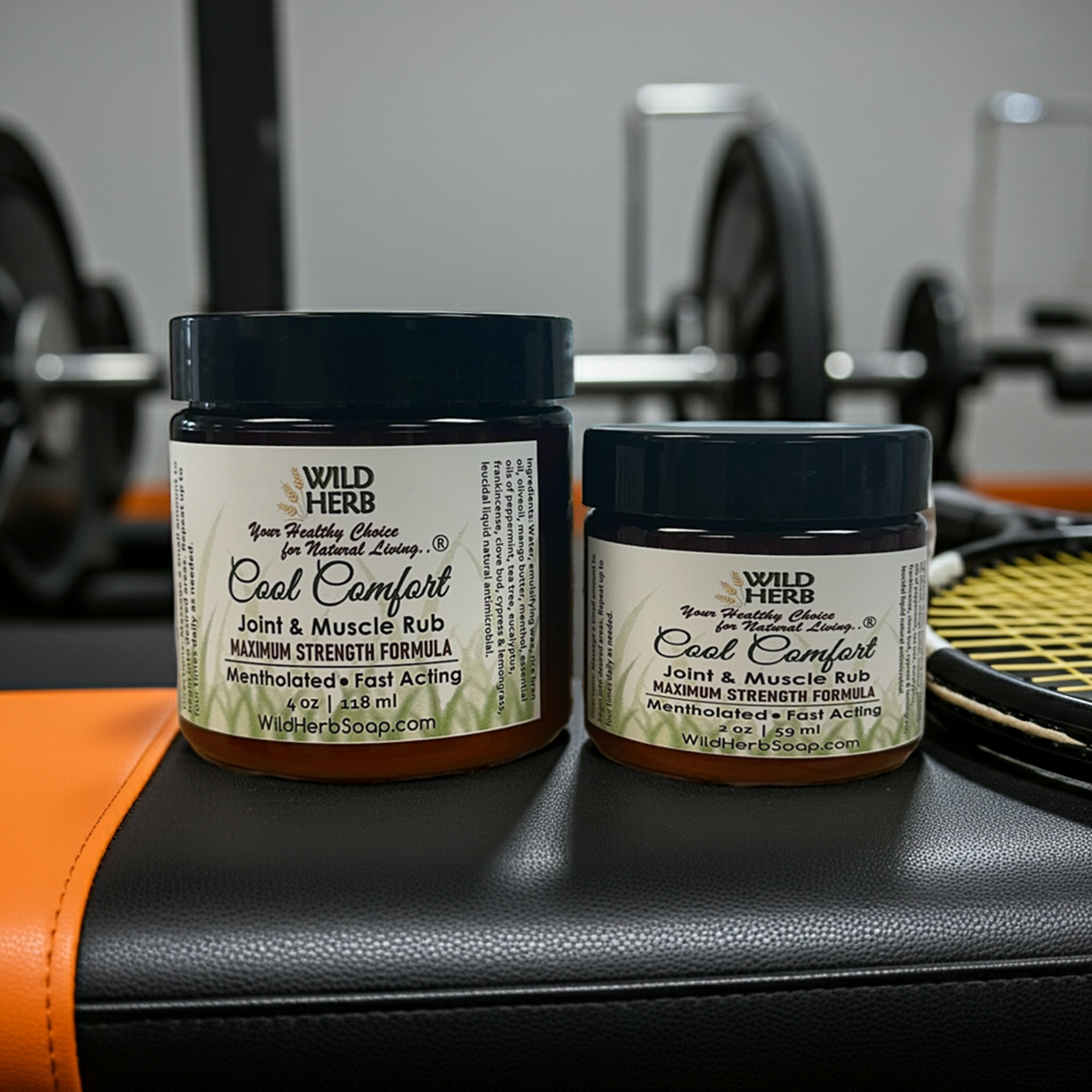 Two jars of Wild Herb Cool Comfort Joint & Muscle Rub on a gym bench with gym equipment in the background.